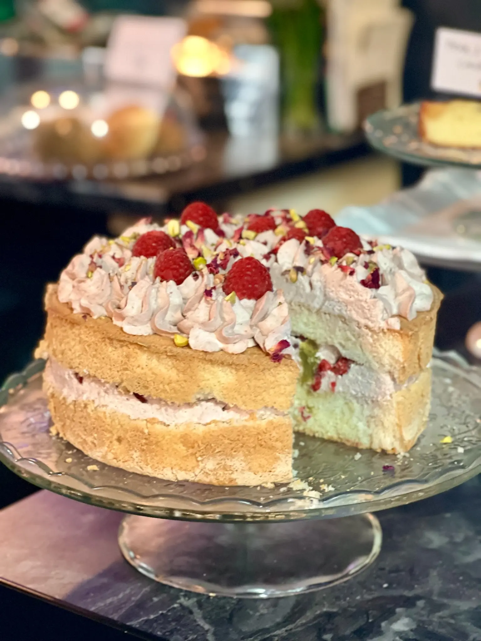 Raspberry and pistachio layer cake on a glass cake stand