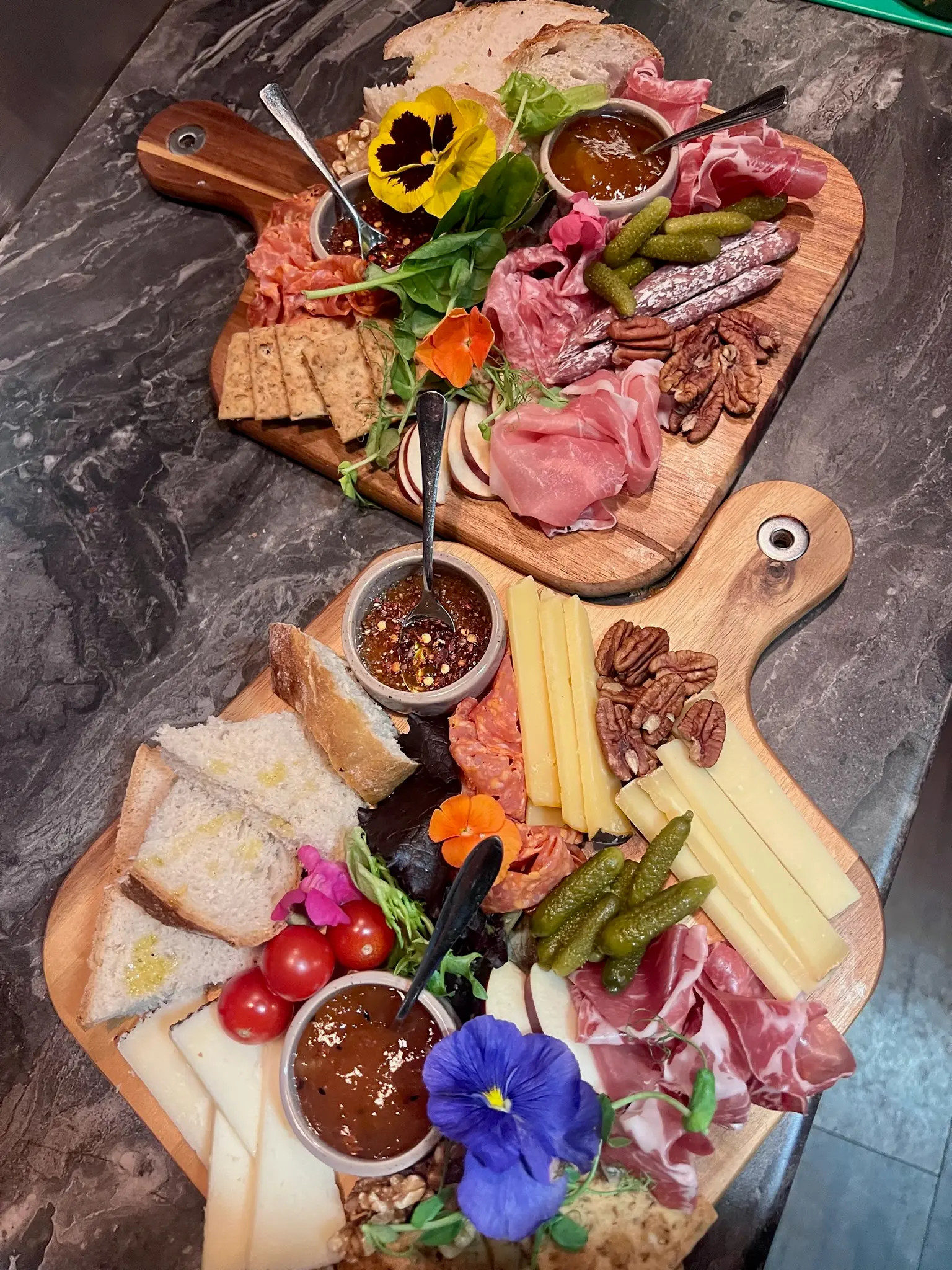 Two charcuterie boards with cured meats, cheese and edible flowers